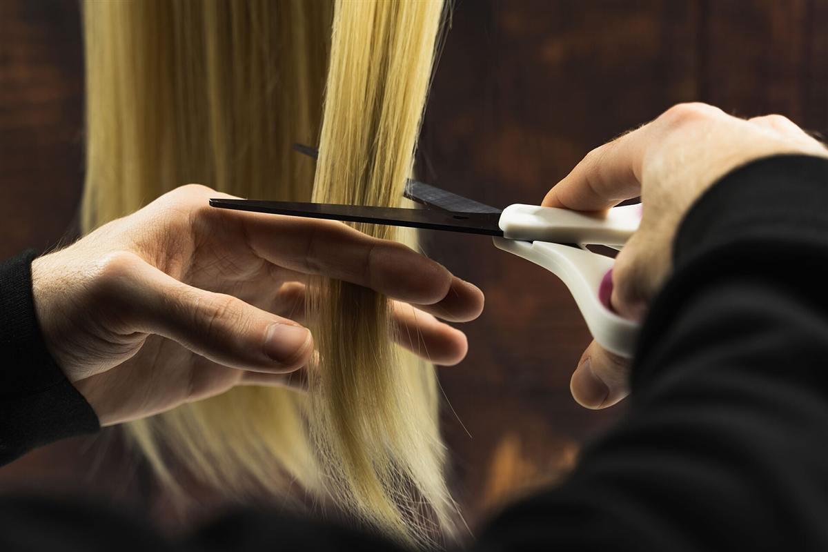 Des ciseaux coupent une mèche de cheveux blonds.
